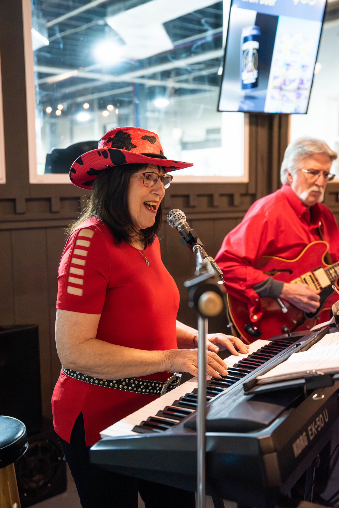 Beverly singing at the keyboard in a red hat and sequined top