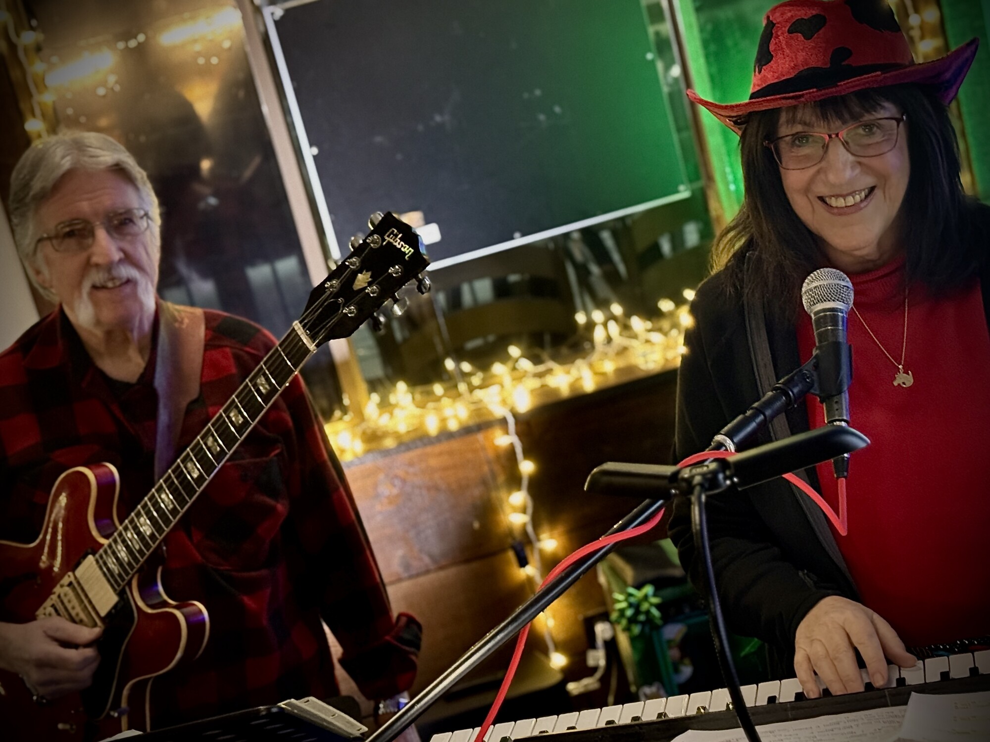 Charlie and Beverly playing a holiday show with string lights behind them