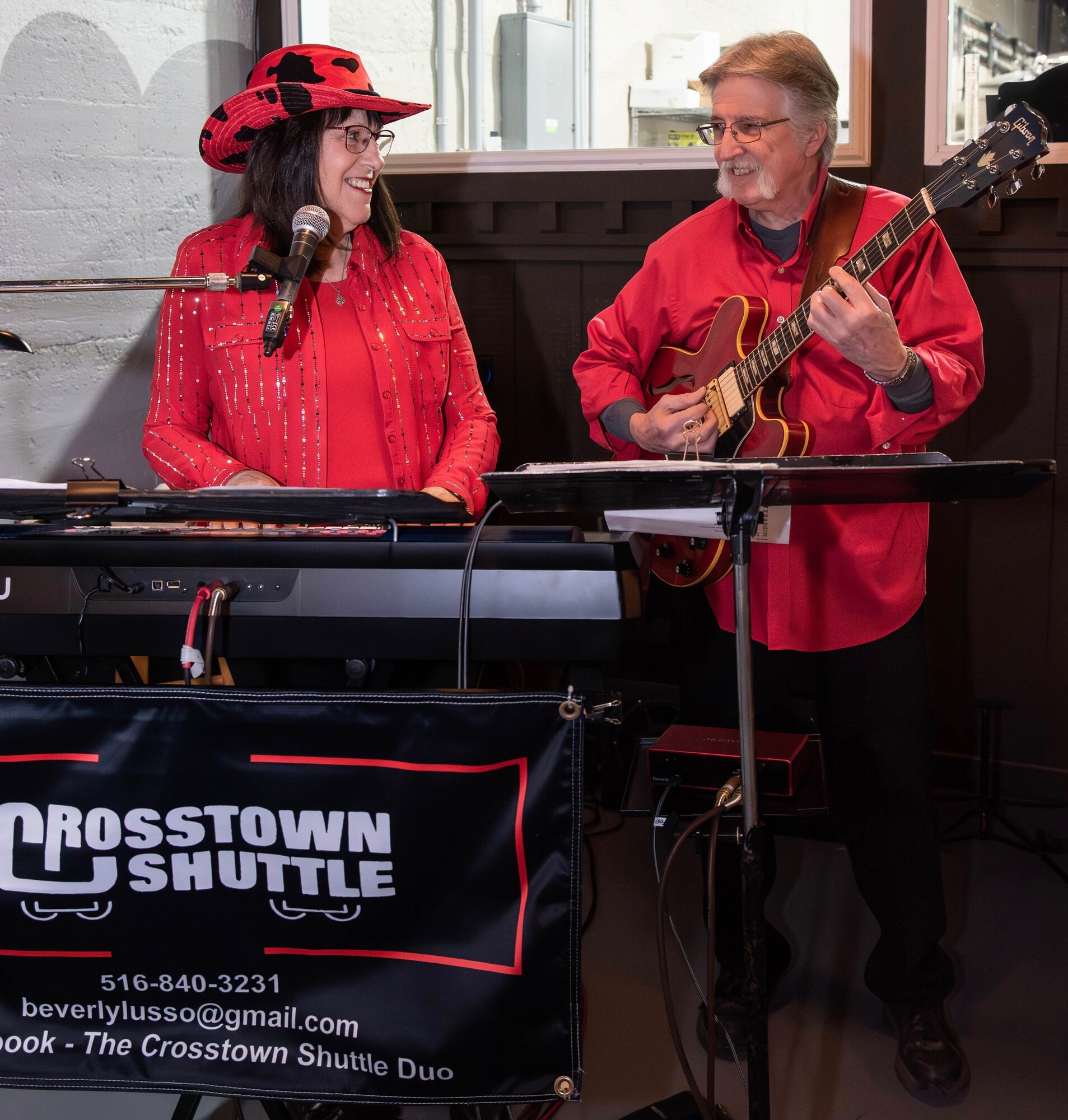 Charlie and Beverly performing in matching red outfits behind the Crosstown Shuttle banner