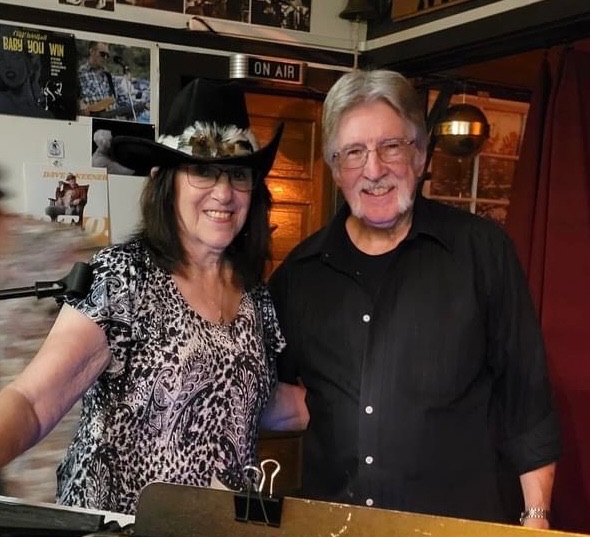 Charlie and Beverly smiling together under the ON AIR sign at a radio spot