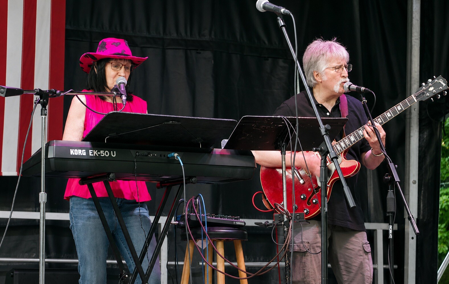 Charlie and Beverly on an outdoor stage with an American flag behind them